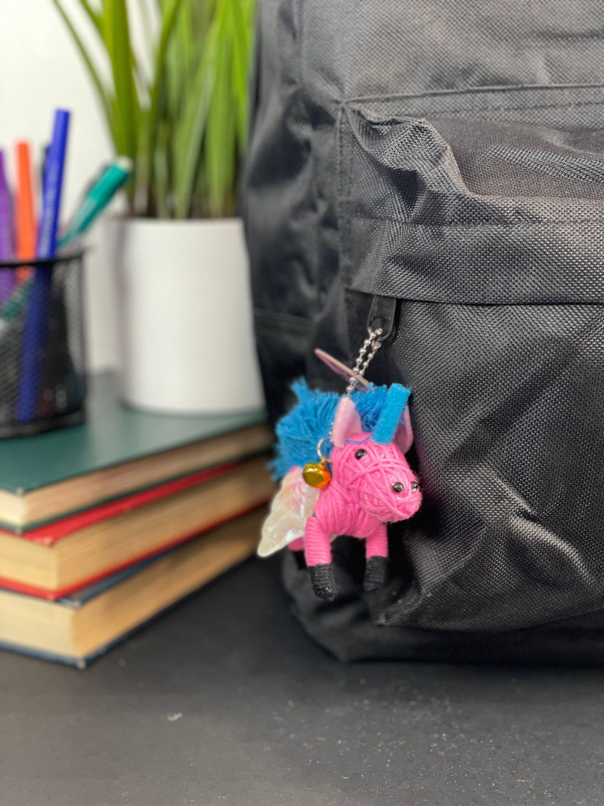 Pink yarn unicorn keychain hanging from black backpack.