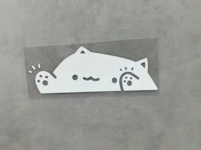 White cat-shaped sticker with cute face and ears on gray background.